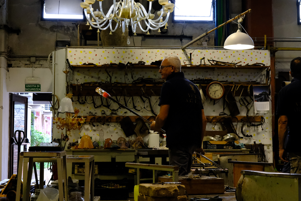 Glass blower with initial bead of molten glass, about to add coloring before forming the body of a pitcher