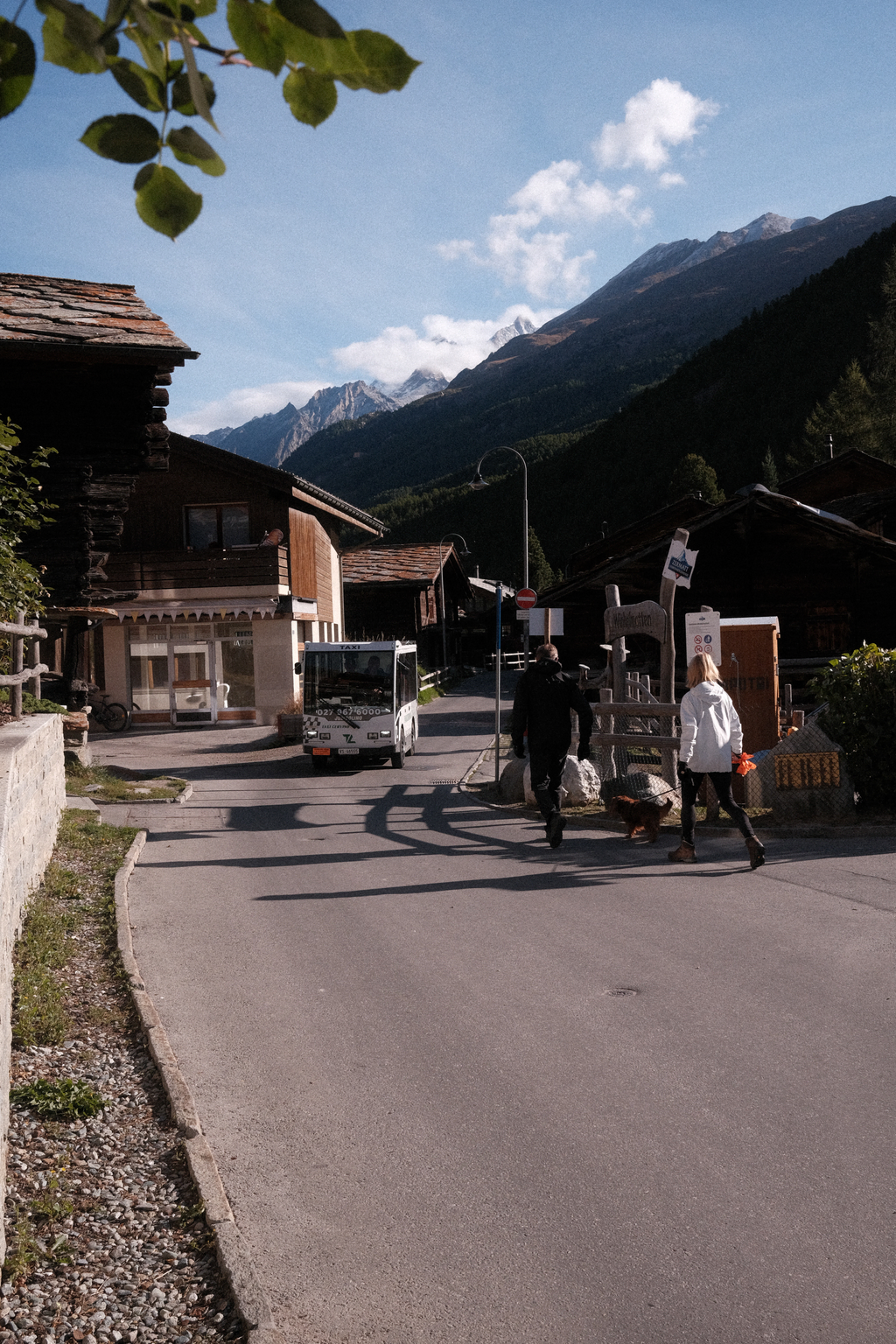 A side street in the morning light, with an "electric brick" taxi and pedestrians passing by