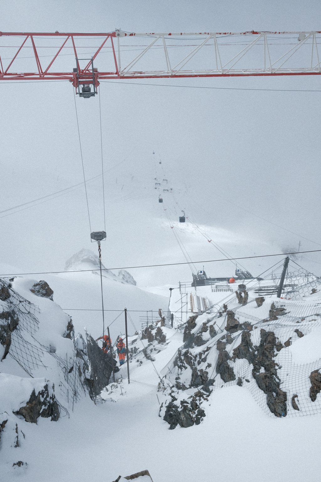 Workers inspecting something on the side of Zermatt Glacier Paradise, being supported by a crane-gantry