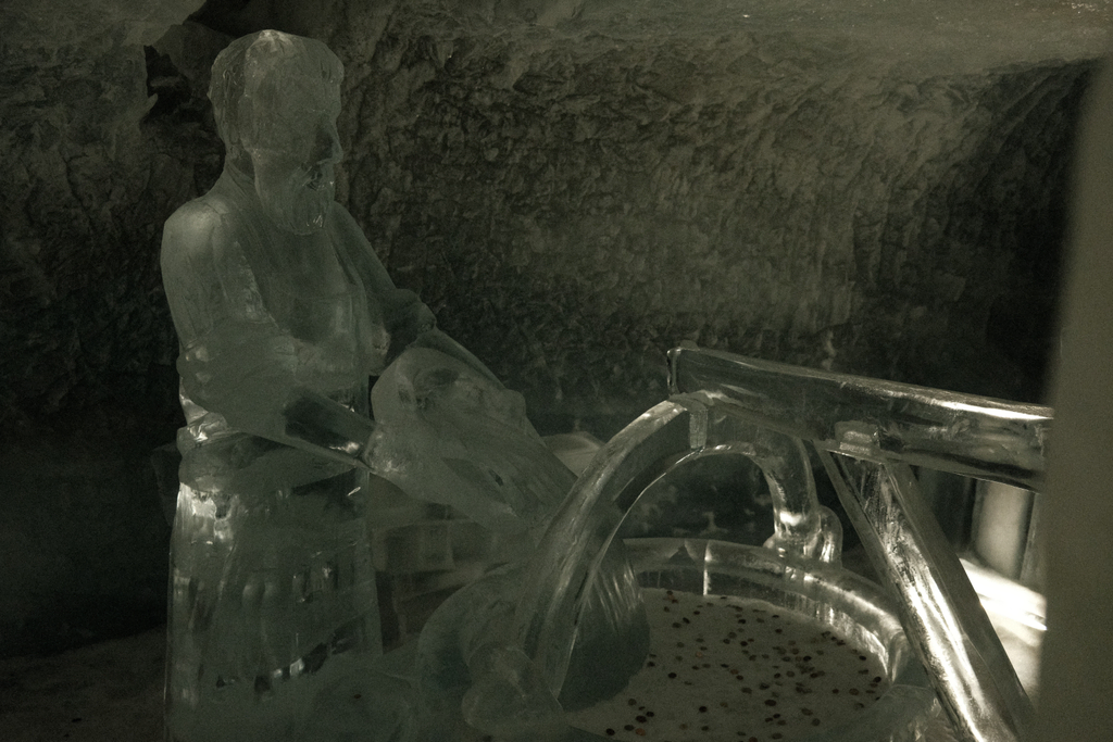 An ice sculpture of a man using a well, the well is full of a variety of currencies