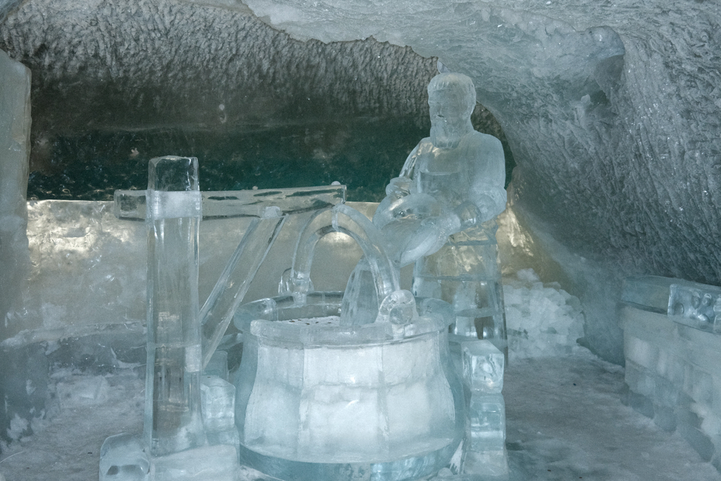 An ice sculpture of a man using a well, the well is full of a variety of currencies