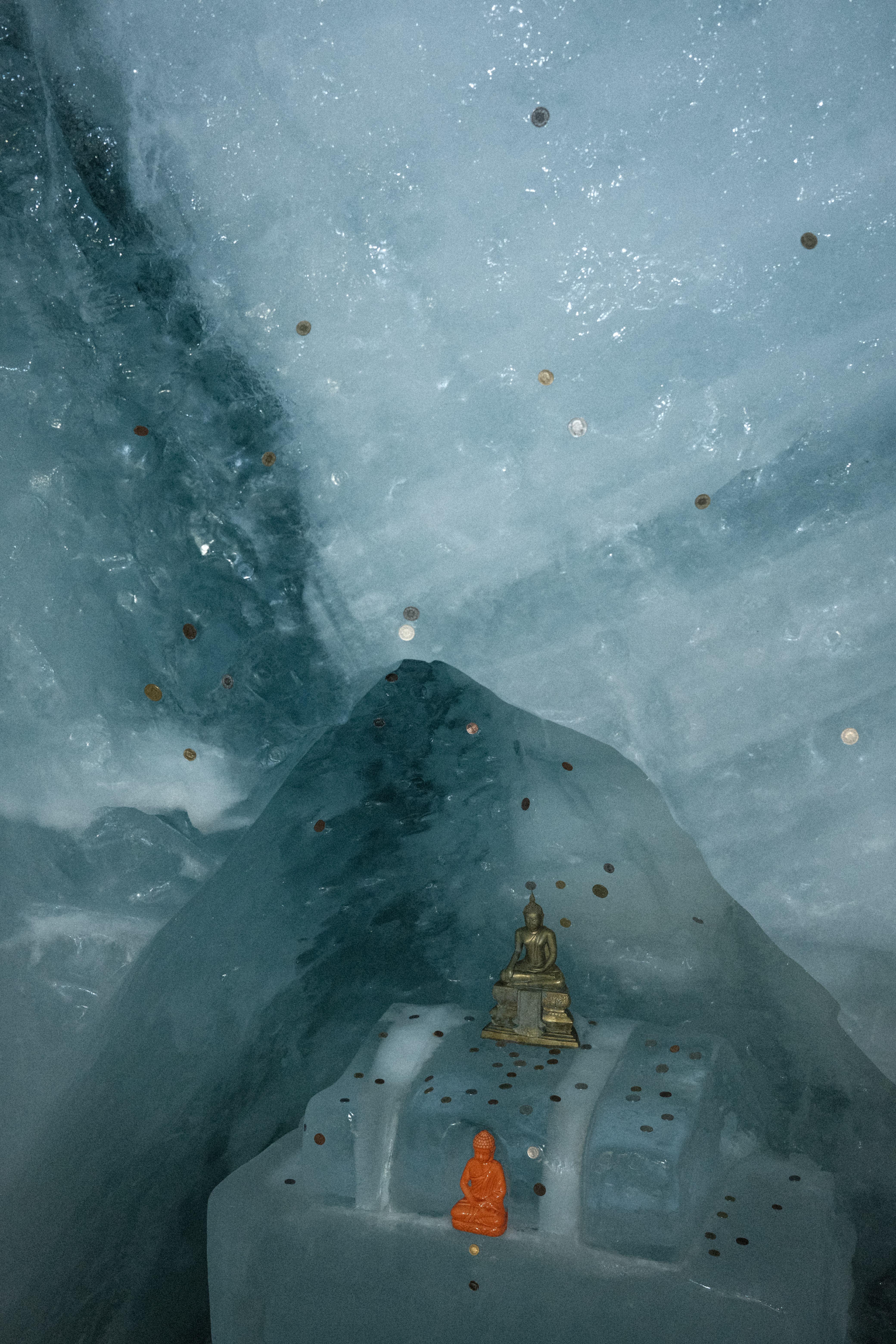 A Buddha statue with coins pressed into the ice surrounding it