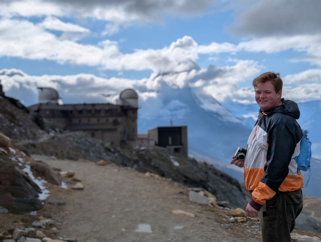 Sean holding his camera with Gornergrat observatory and a partially-obscured Matternhorn in the distance